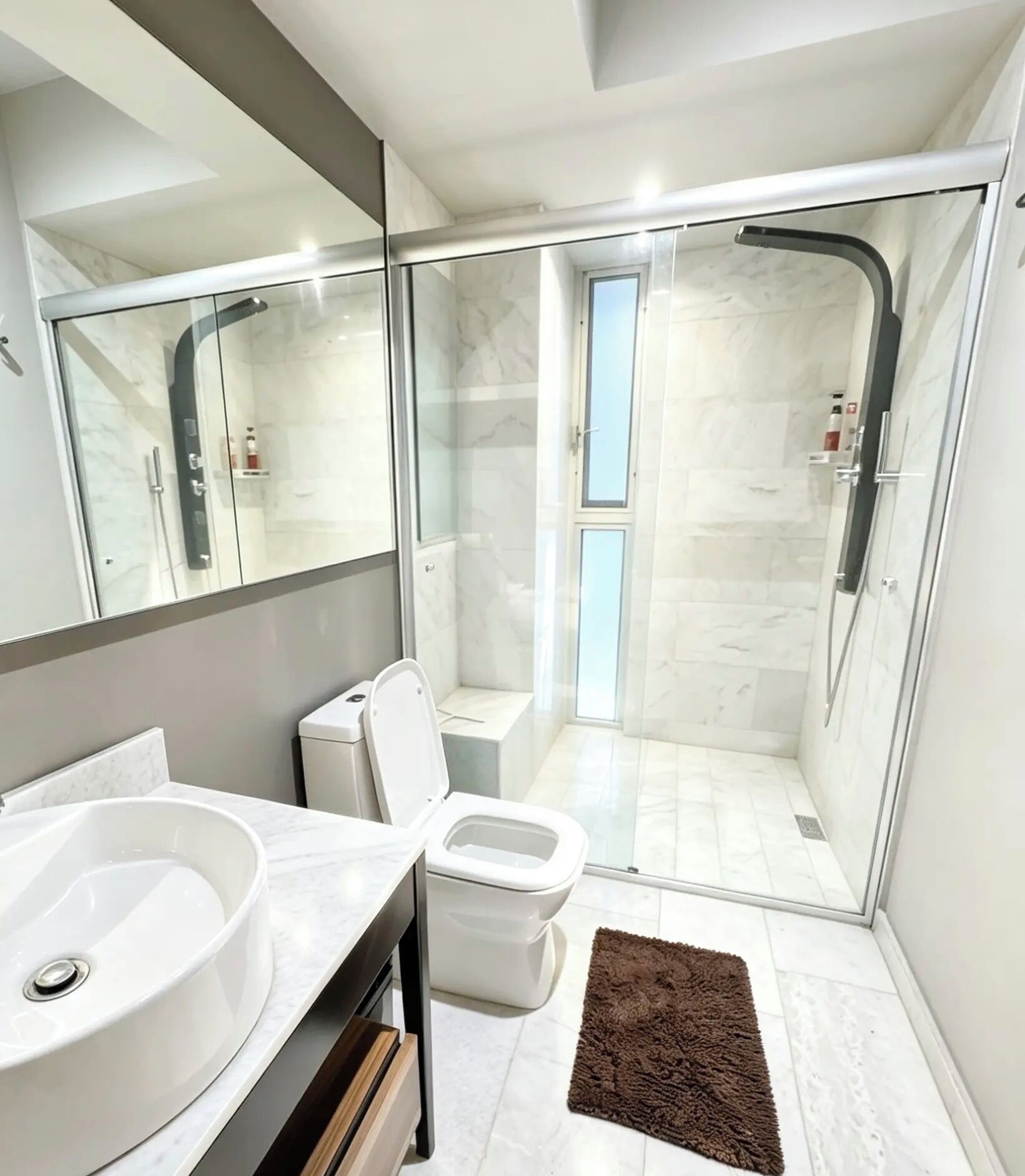 Un baño moderno con cabina de ducha de vidrio, un lavamanos blanco y un inodoro.