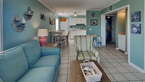 A living room with a blue sofa, a striped armchair, and a coffee table with a basket. - Pam's Paradise (Carolina Beach)