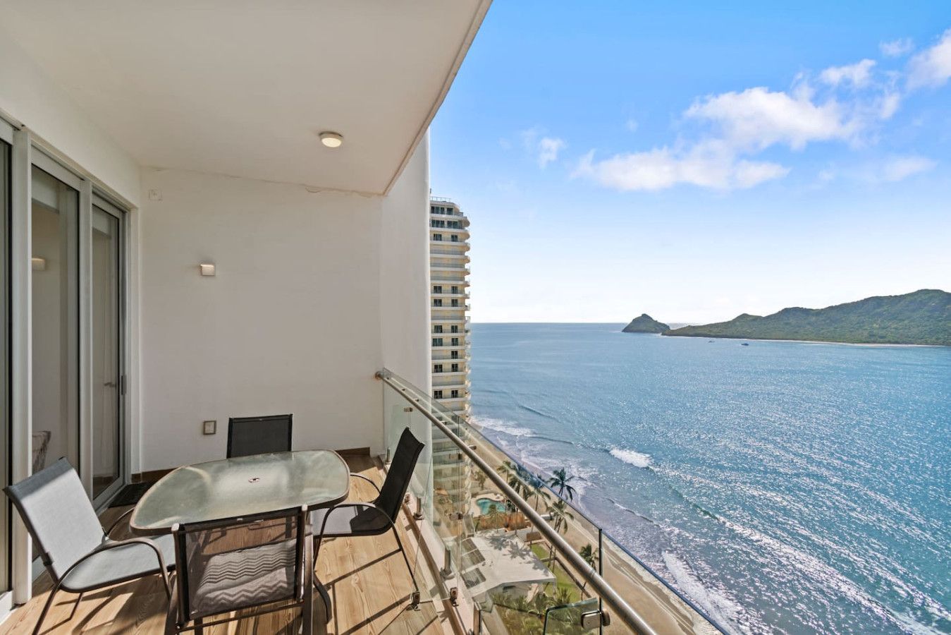 A balcony with a table and chairs, overlooking a beach and ocean.