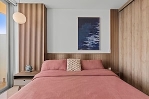 A bedroom with a bed, a nightstand, a wall-mounted lamp, and a framed picture. - 15th Floor Camino al Mar | Beach Front | King Bed (Mazatlán)