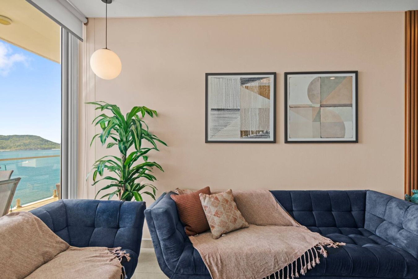 A room with two dark blue sofas, a large potted plant, and two framed abstract artworks on the wall.