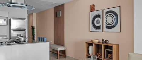 Una cocina moderna con una isla central, comedor con mesa de vidrio y dos obras de arte enmarcadas en la pared.