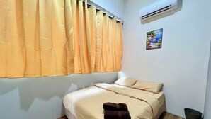 Un letto singolo con copriletto color beige, un asciugamano marrone e una finestra con tende gialle.