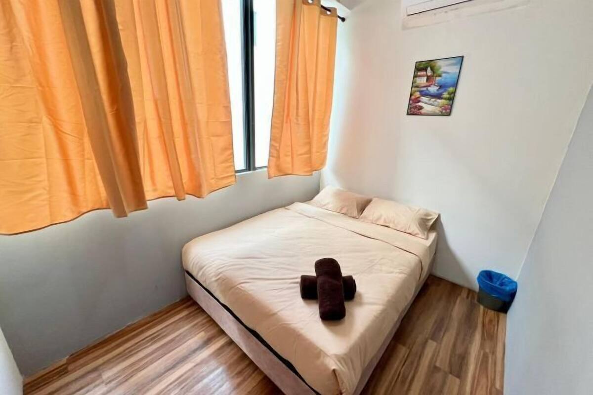 Une petite chambre à coucher, bien rangée, avec un lit, une fenêtre avec des rideaux, un climatiseur fixé au mur et une petite poubelle.