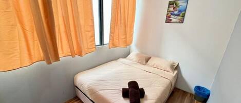 Um quarto pequeno e bem arrumado com uma cama, uma janela com cortinas, um ar condicionado fixado na parede e uma pequena lixeira.