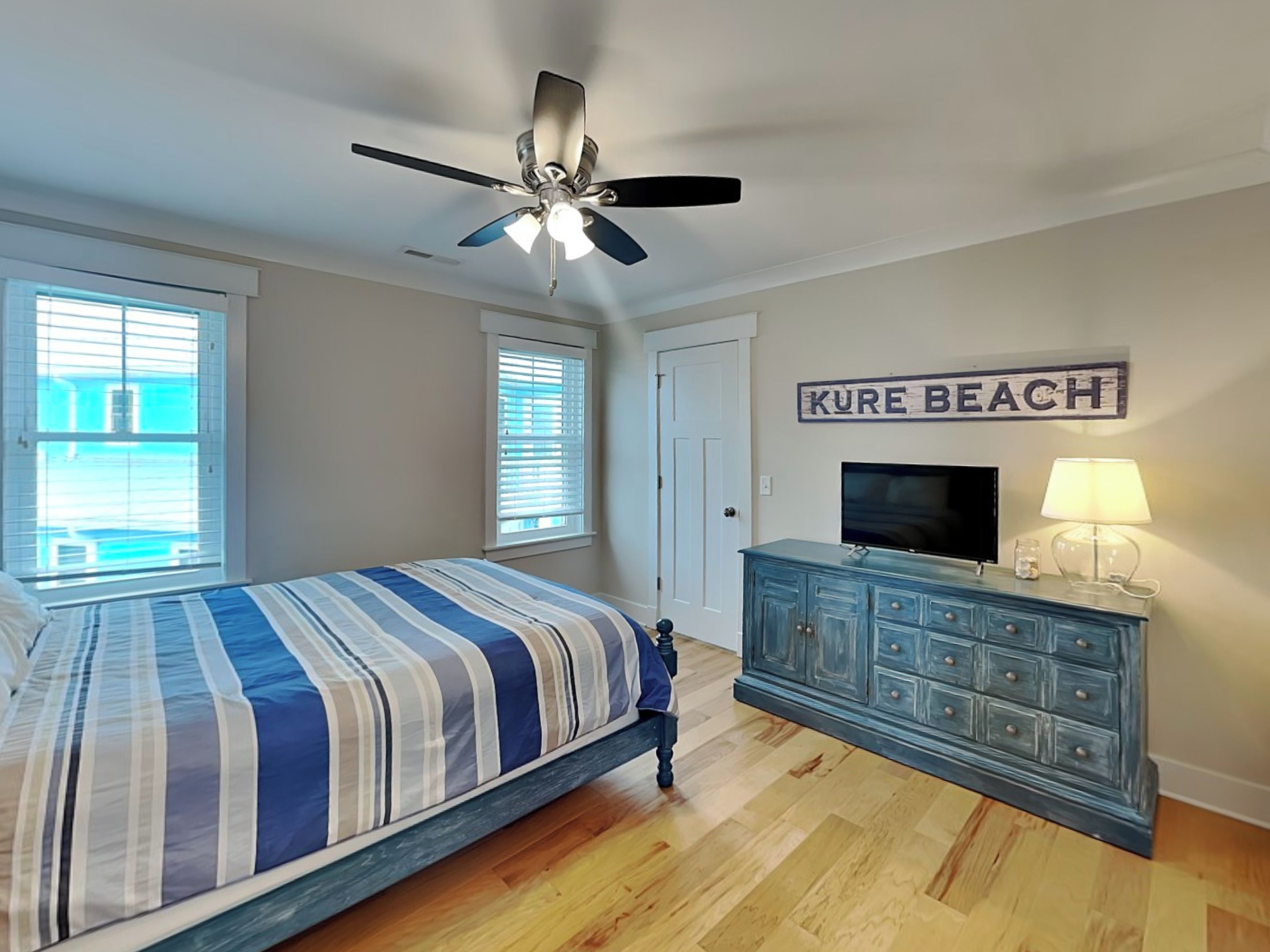 Un dormitorio con cama, ventilador de techo, cómoda, televisor y un letrero que dice "KURE BEACH".