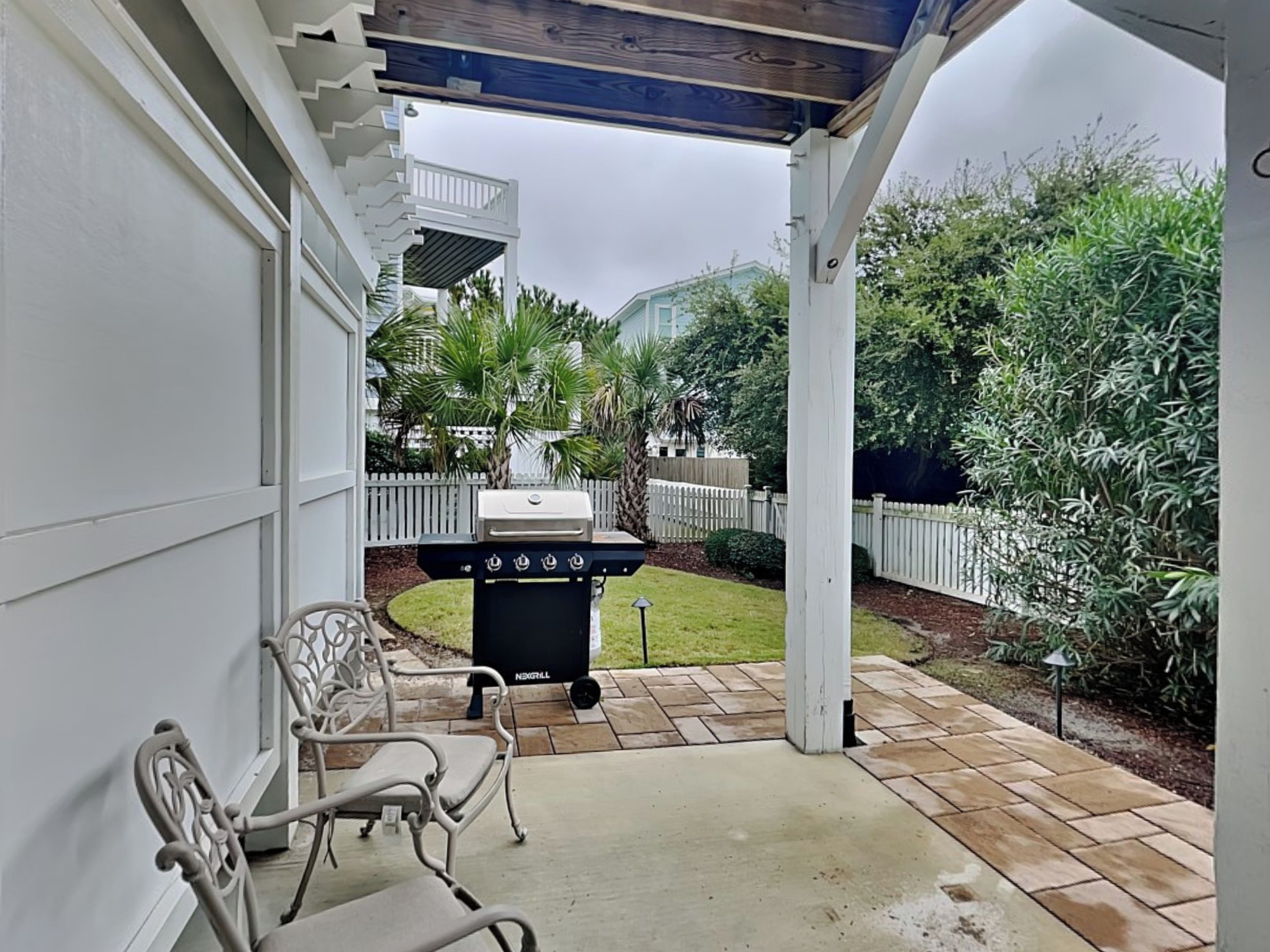 A covered patio area with a grill, chairs, and a view of a residential neighborhood.