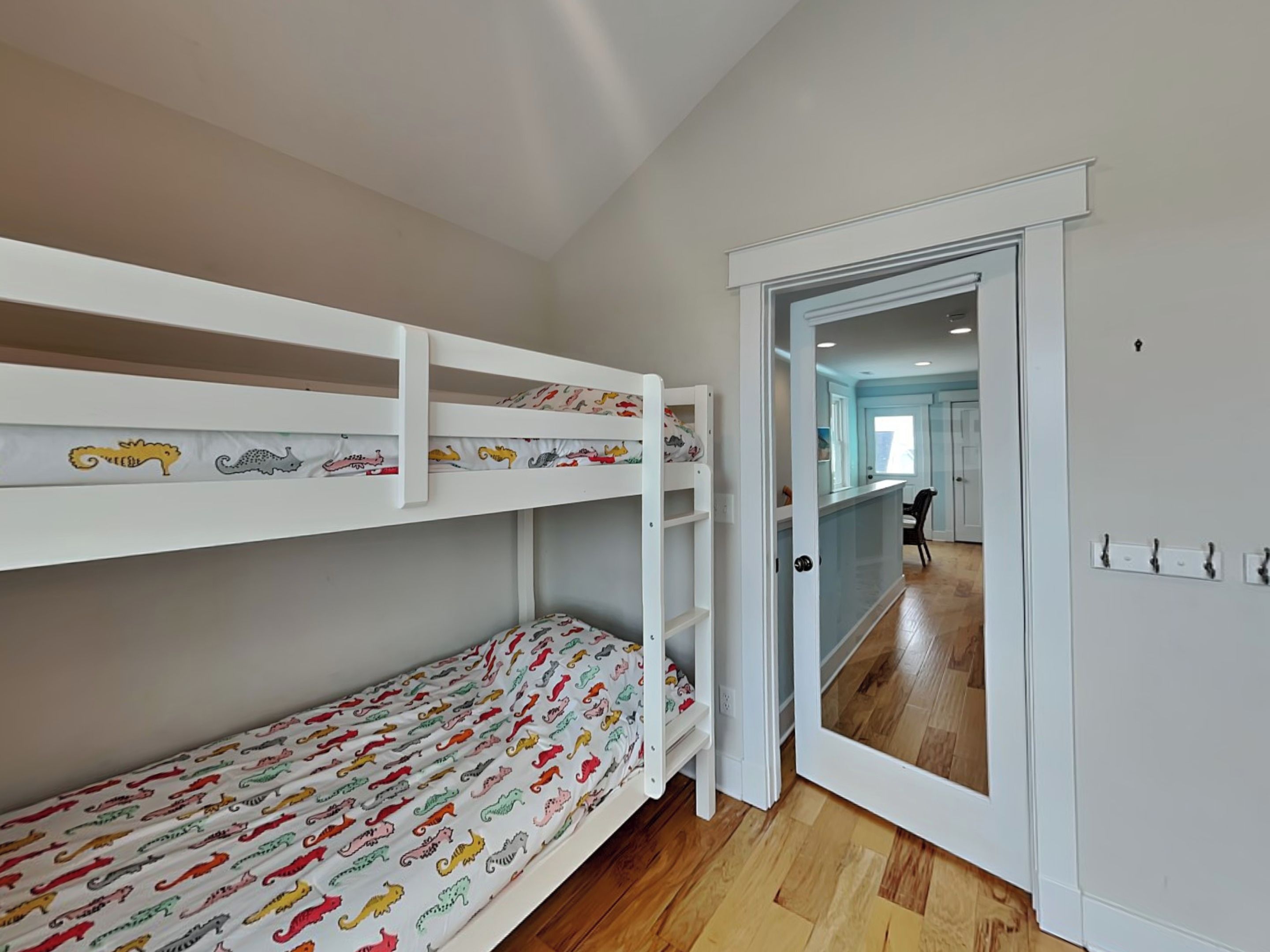 A room with a bunk bed, a door leading to another room, and a visible kitchen area.