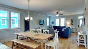 A spacious living area with a dining table, chairs, a blue sofa, and a ceiling fan. - Seahorse by the Sea (Kure Beach)