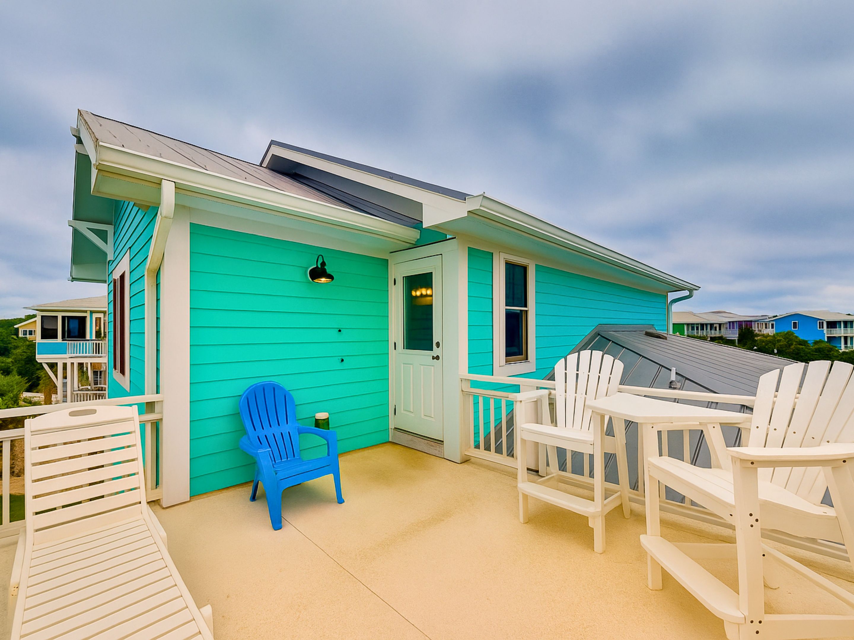 A turquoise house with a porch, white chairs, and a blue chair.