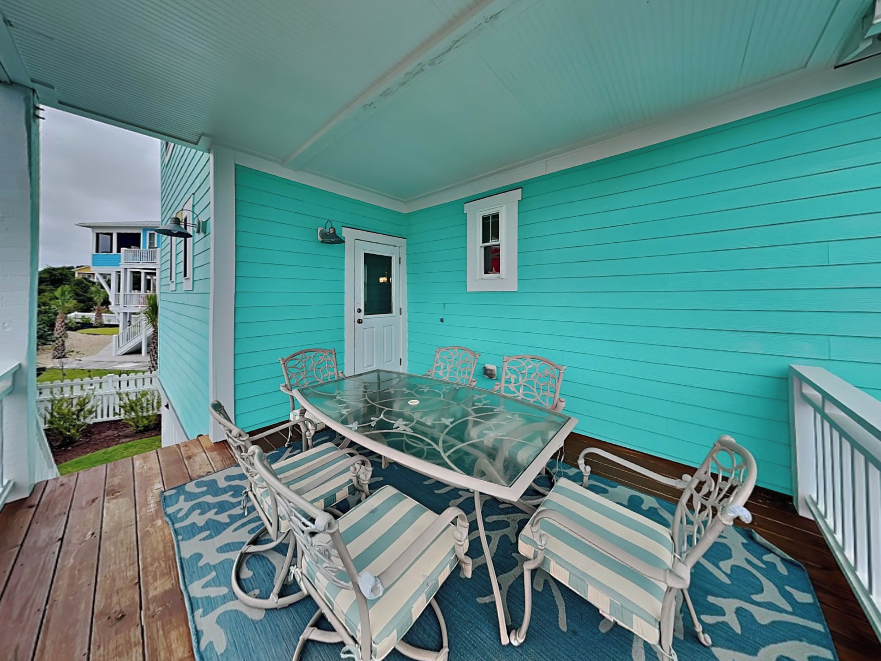 Une véranda aux murs turquoise, avec une table à plateau de verre et des chaises à rayures.