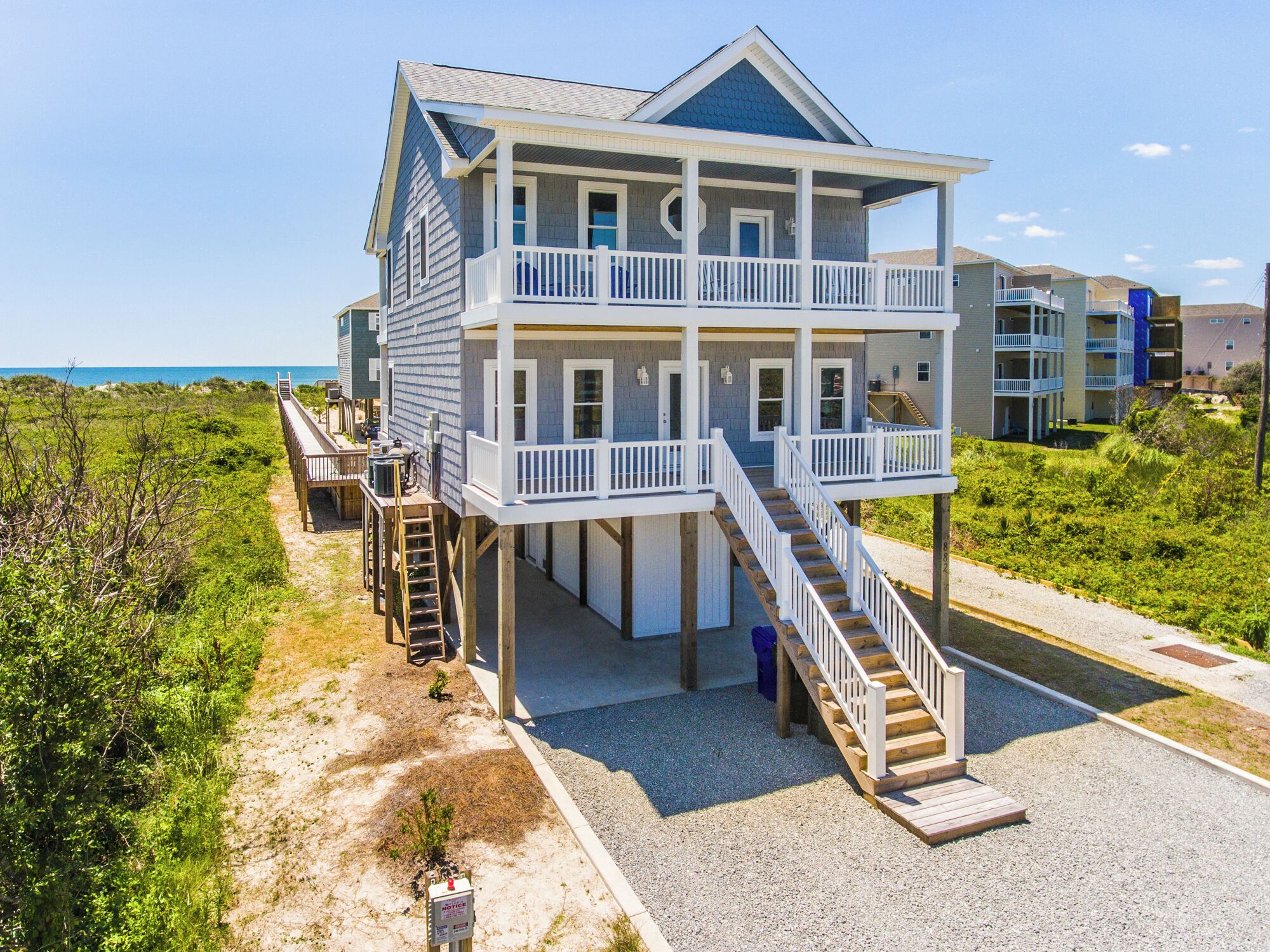 Ein mehrstöckiges Strandhaus mit Balkon, Treppe und Blick aufs Meer.