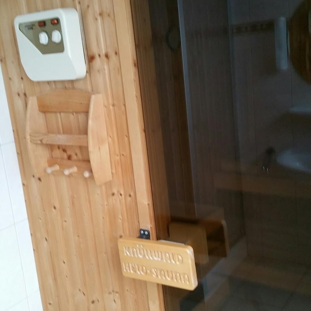 Een houten wand met een bedieningspaneel en een bord waarop 'Kühlwald Heli-Sauna' staat.