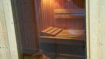 Eine Sauna mit Holzwänden und -bänken, einem sichtbaren Türgriff und einem Schild, das anzeigt, dass es sich um eine 'Knüwalld Heil-Sauna' handelt.