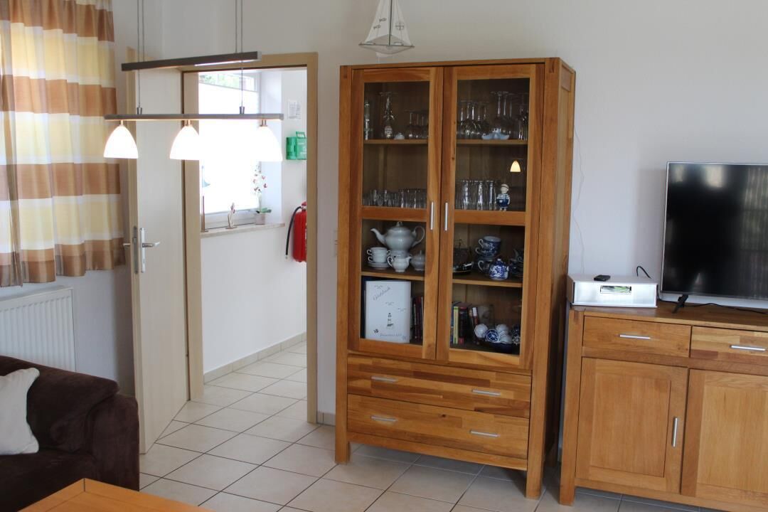 Ein Wohnzimmer mit einer Holzkabine, die Glaswaren beherbergt, einem Fernseher auf einem Holzständer und einem braunen Sofa.