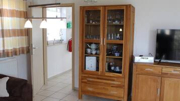 Ein Wohnzimmer mit einer Holzkabine, die Glaswaren beherbergt, einem Fernseher auf einem Holzständer und einem braunen Sofa.
