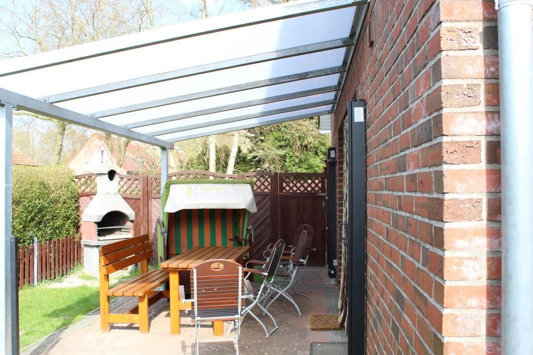 Eine Terrasse im Freien mit einer Ziegelwand, einem Holztisch, Metallstühlen und einem Pizzaofen.