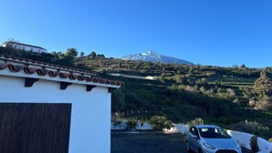 Un bâtiment blanc avec un toit recouvert de tuiles, une voiture garée et une montagne en arrière-plan.