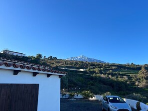 Ein weißes Gebäude mit Ziegeldach, ein geparktes Auto und ein Berg im Hintergrund.