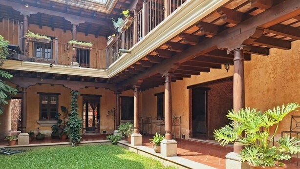 Un patio con una pérgola de madera, plantas en macetas y una zona verde.