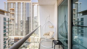A balcony with a hanging chair, a glass table, and a view of high-rise buildings. - Stylish Downtown Studio w/ Pool & Gym Access (Dubai)