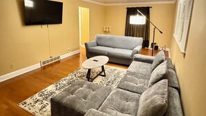 A living room with a sectional sofa, a flat-screen TV mounted on the wall, a small round table, and a patterned rug. - Cozy house in Bridgeport WV - 5 Bedrooms (Bridgeport)