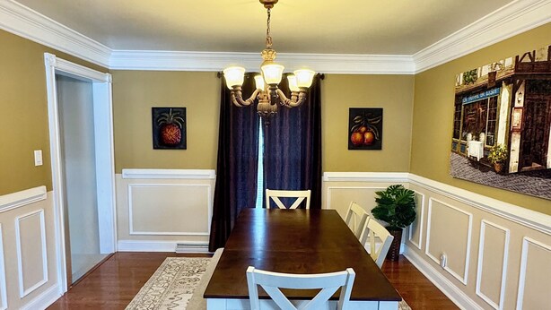 A dining room with a dark wooden table, white chairs, a chandelier, and patterned rugs. - Cozy house in Bridgeport WV - 5 Bedrooms (Bridgeport)