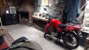 Uma motocicleta estacionada em um ambiente rústico com paredes de pedra, lareira e mesa de madeira.