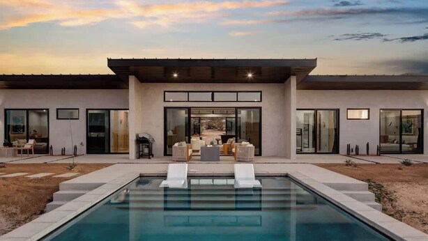 Et moderne hus med pool, store vinduer og en patio.