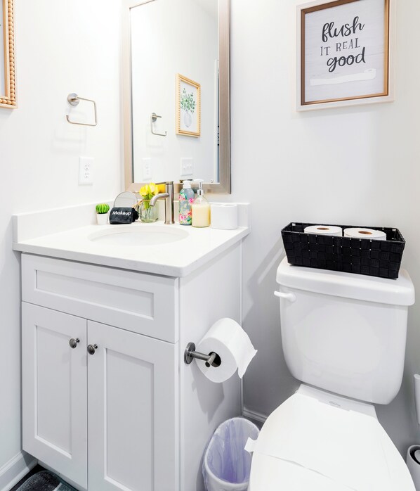 A bathroom with a white sink, mirror, toilet, and a trash bin. - 8BR Near Southend/Uptown w/GameRoom/HotTubs/Fenced (Charlotte)
