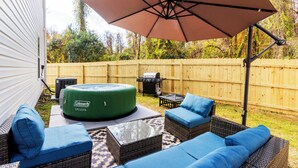 Een achtertuin met een Coleman Saluspa bubbelbad, rieten meubels en een grote parasol.