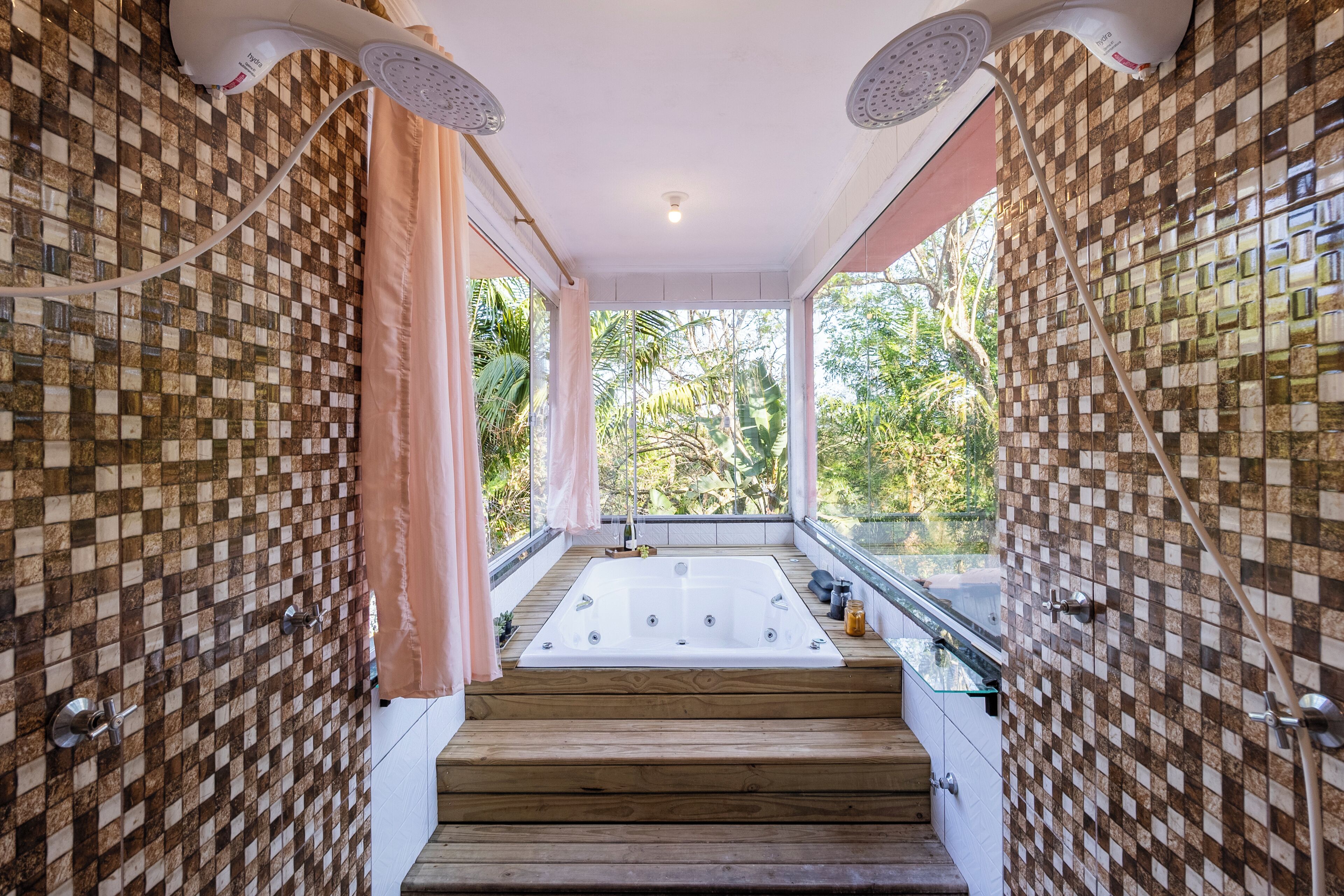A modern bathroom with a checkered mosaic wall, a wooden floor leading to a large bathtub, and a glass shower enclosure.