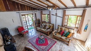 A spacious living area with a wooden ceiling, a red rug, and a sofa with colorful cushions.