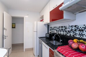 Eine moderne Küche mit weißen und roten Schränken, einer schwarzen Arbeitsplatte und einer gefliesten Spritzschutzwand.