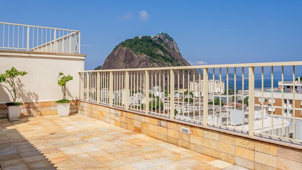 A rooftop terrace with a railing, potted plants, and a view of a mountain and cityscape. - Sunset Urca - Conforto e lazer (Rio de Janeiro)