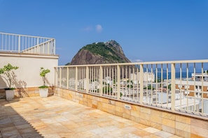 Une terrasse sur le toit, dotée d’une balustrade, de plantes en pot et offrant une vue sur une montagne et le paysage urbain.