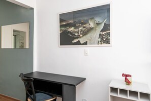 Een kamer met een donker houten bureau, een stoel, een witte plank en een lijstwerk met een stadsgezicht aan de muur.