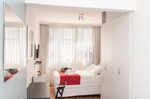 Ein modernes Hotelzimmer mit Bett, Schreibtisch, Stuhl, Fernseher und Kleiderschrank.