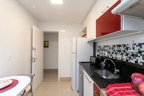 Een compacte keuken met witte kastjes, een zwart aanrechtblad, een betegelde spatwand en een rode muur.