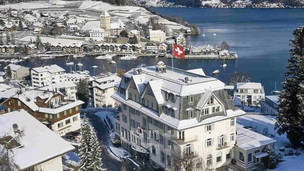 A snow-covered town with a prominent building featuring a tower, a marina with boats, and a lake in the background. - Lakefront Apartment in Spiez Bay (Spiez)