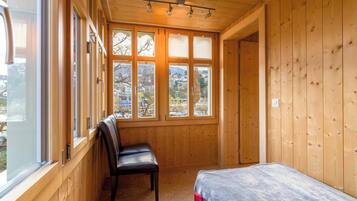 Ein Zimmer mit Holzboden, einem Bett, einem Sessel und großen Fenstern.