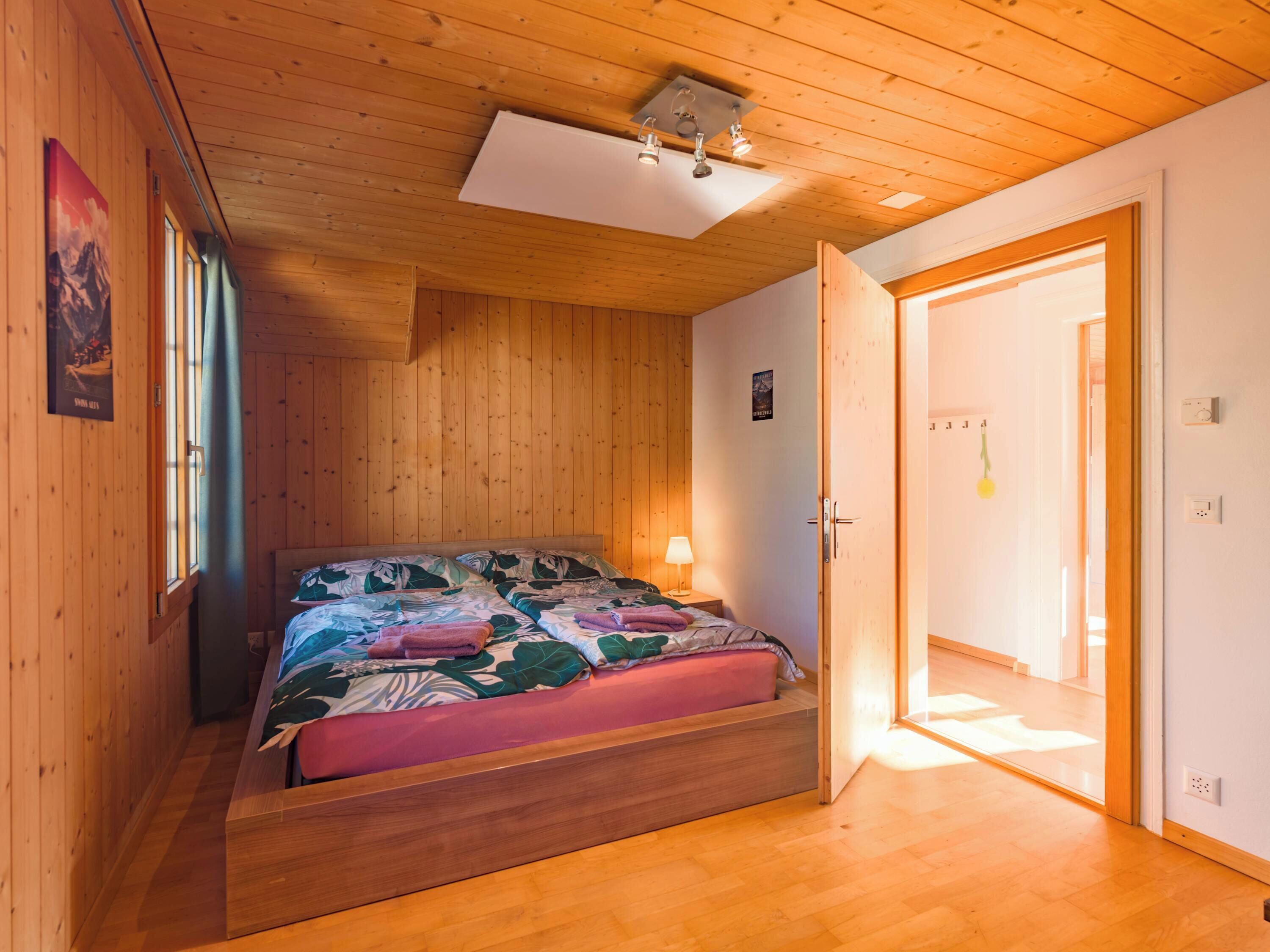 Une chambre à coucher dans une cabane en bois, avec un lit, une table de chevet, une lampe et une porte donnant sur une autre pièce.