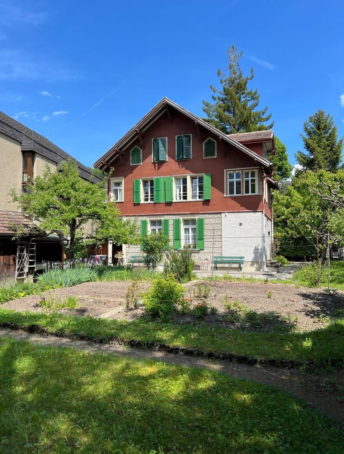 A two-story house with green shutters, a front yard, and a wooden fence.