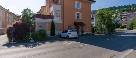A residential building with a white car parked in front, a visible garage door, and a clear sky.