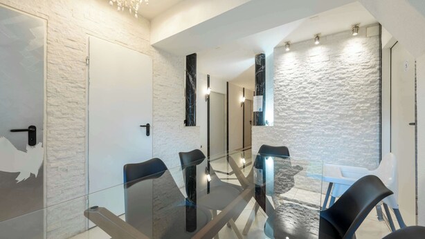 Una sala de conferències moderna amb taules de vidre i cadires negres, parets de maó blanc i una paret d'accent amb textura de pedra.