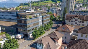 Un edifici residencial de diversos pisos amb teulada plana, una zona d'aparcament i vista a un paisatge muntanyós.