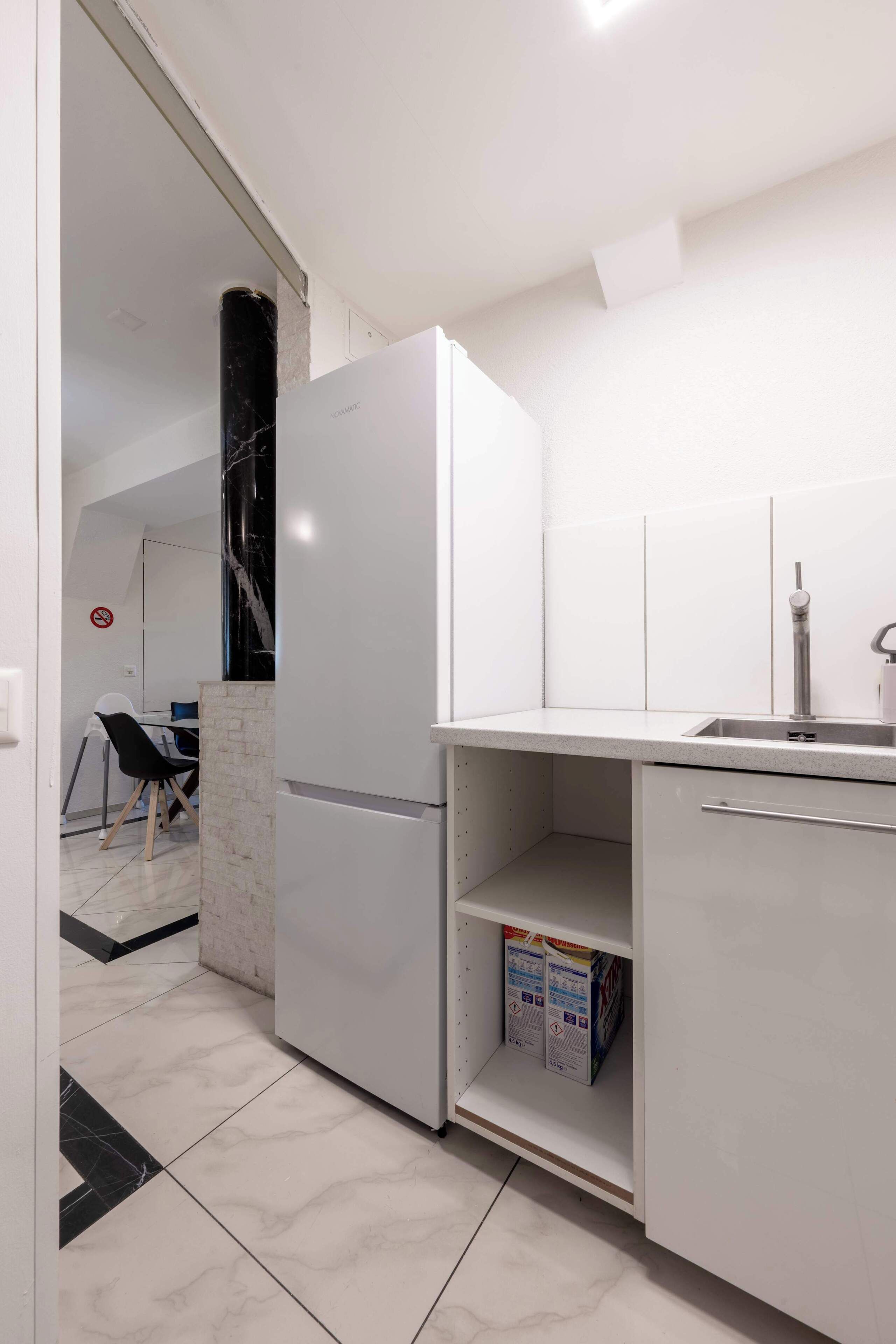 A compact kitchen with white cabinetry, a marble-tiled floor, and a built-in sink.
