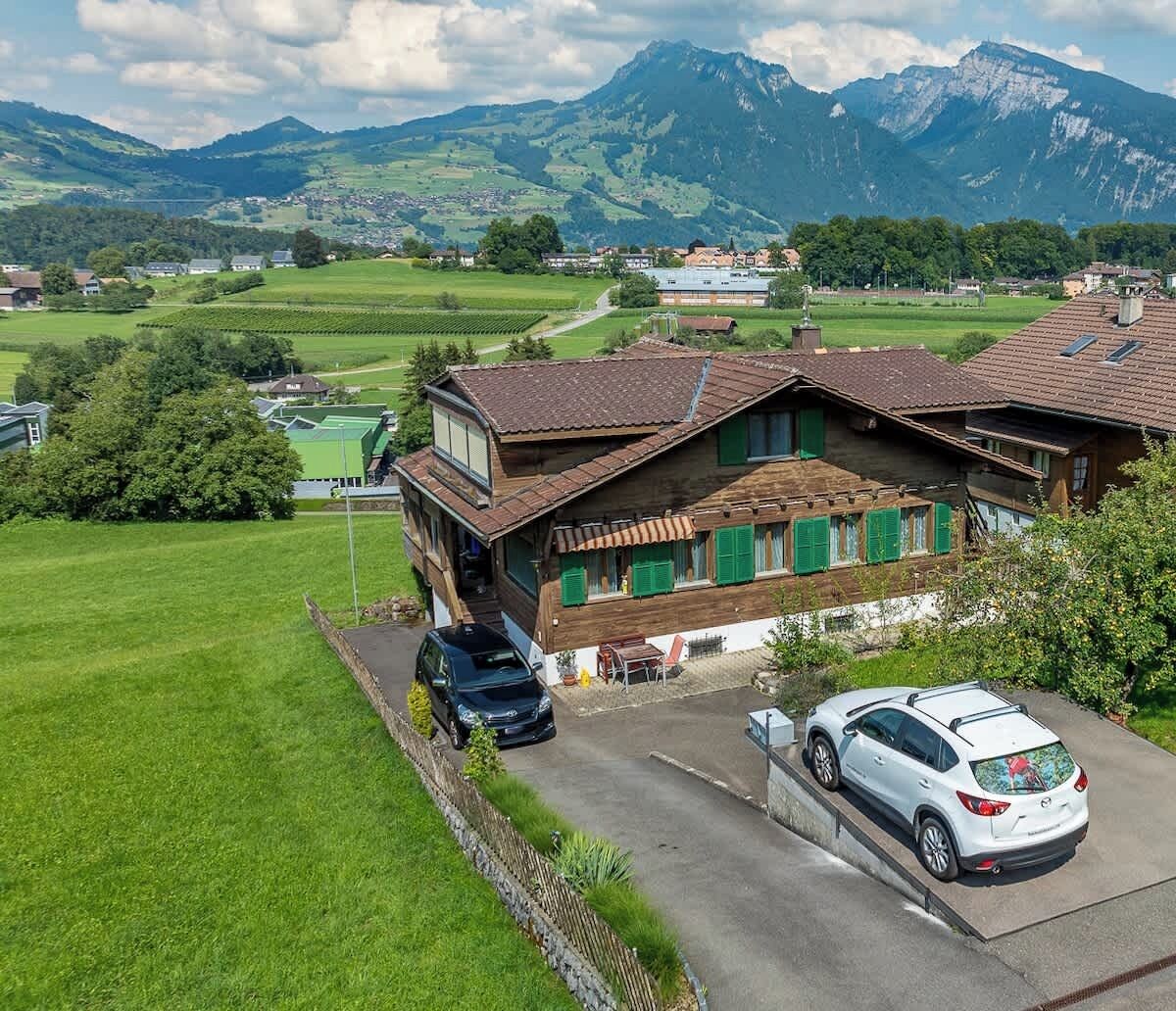 Ein traditionelles Chalet mit schrägem Dach und Holzwand, ein Auto befindet sich auf der Auffahrt.