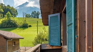 Un balcón de madera con vista a un campo verde y una montaña al fondo.