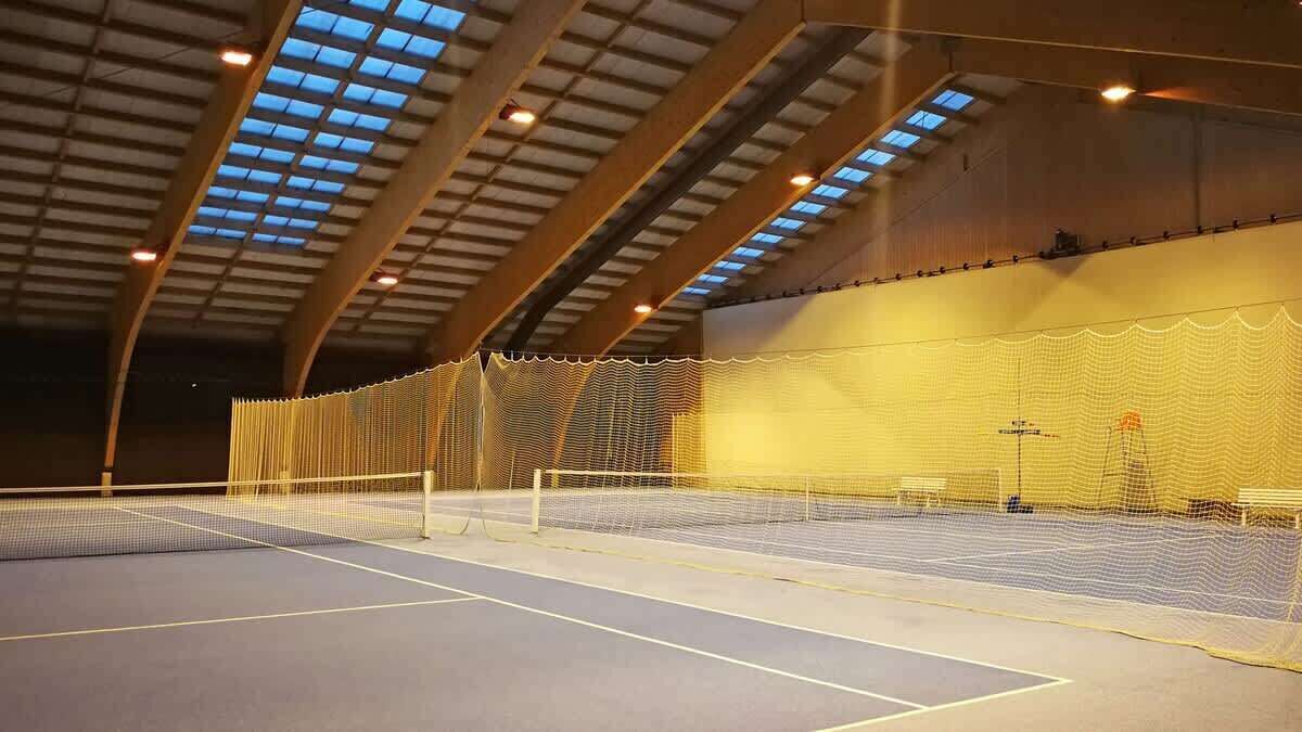 Ein Hallen-Tennisplatz mit Netz, Holzbalken und Oberlichtern.